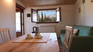 A wooden dining table with a pitcher and cups, a green sofa, and a window with a view of trees and buildings. - All'Antica Mattonata (Assisi)