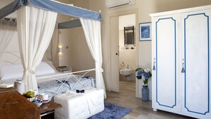 A bedroom with a four-poster bed, a bedside table with a lamp, a wardrobe, and a bathroom visible through an open door. - All'Antica Mattonata (Assisi)