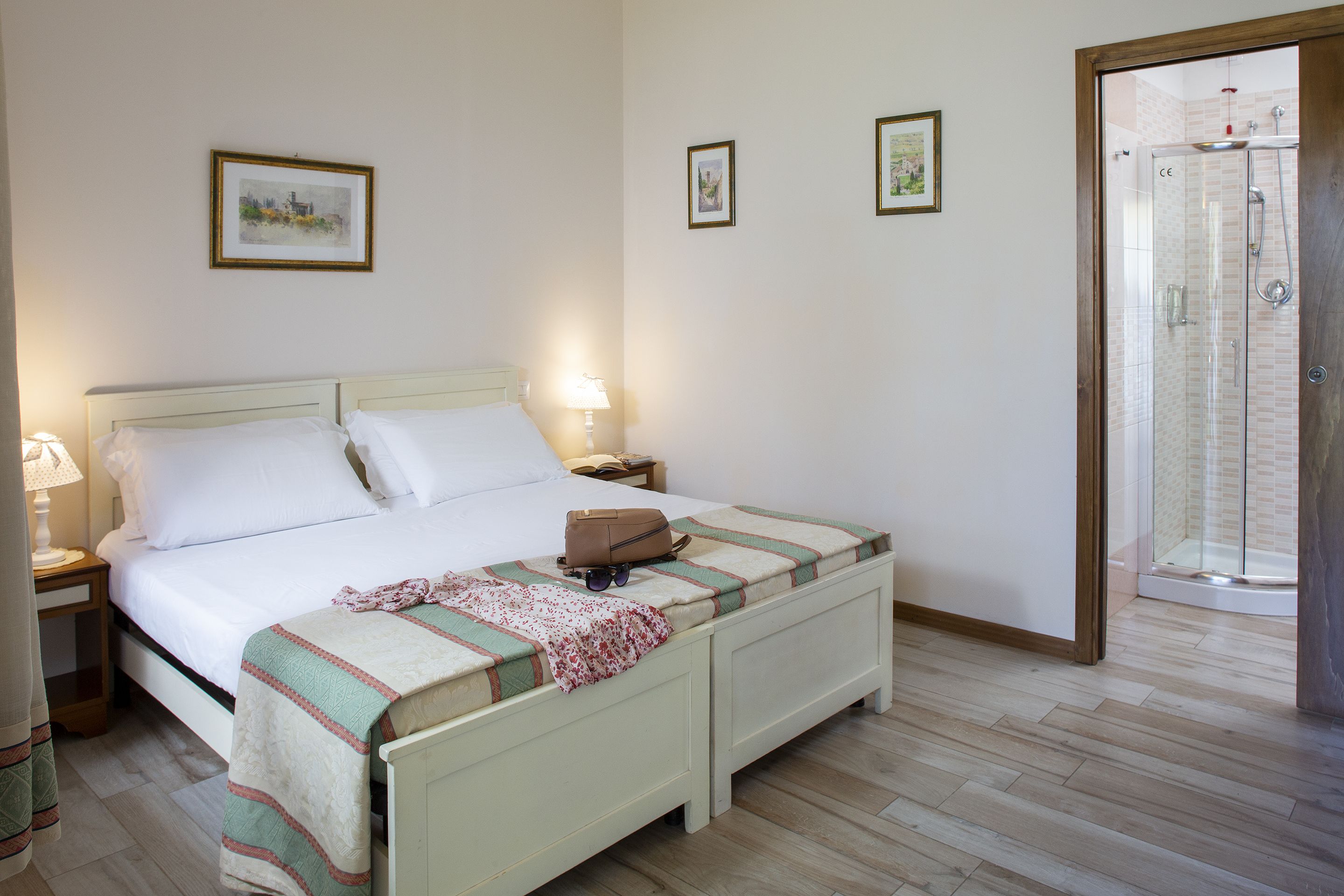 A bedroom with a bed, bedside tables, a nightstand, a wooden floor, and a glass shower door.