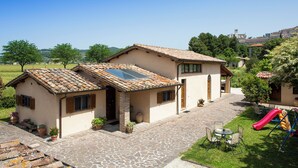 A house with a patio, a play area with a slide, and a view of the surrounding landscape. - All'Antica Mattonata (Assisi)