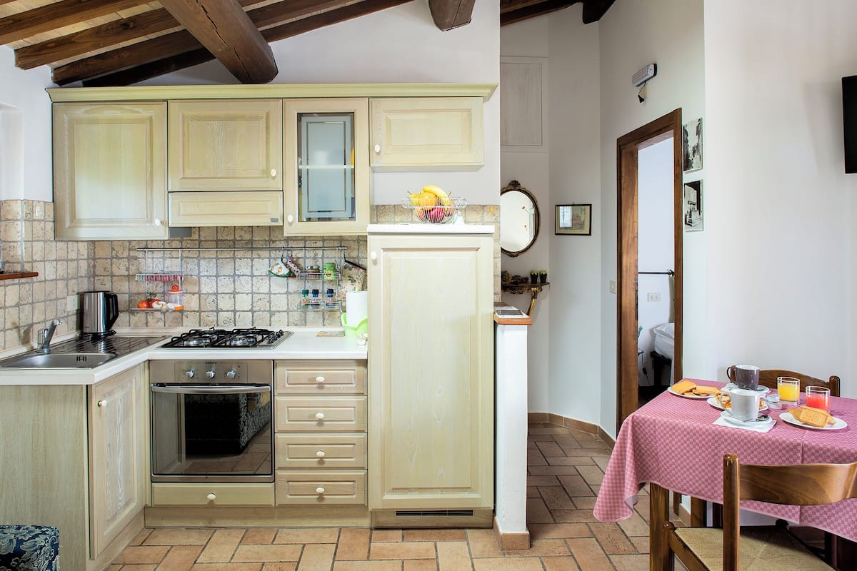 A kitchen with a stove, oven, and cabinets. There is a dining table with a tablecloth and chairs.