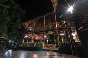 Un espace extérieur aménagé en patio, doté d’une structure de toit en chaume, de sièges et de plantes en pot.