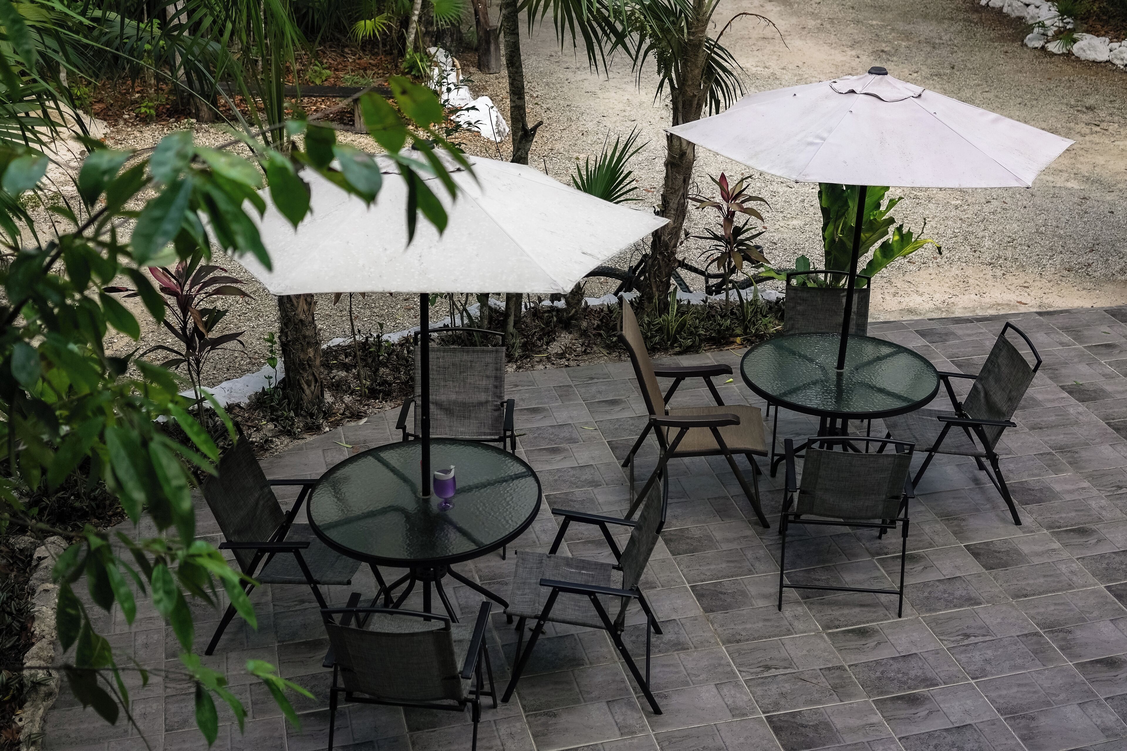 An outdoor patio with round tables and chairs, two umbrellas, and a gravel path.