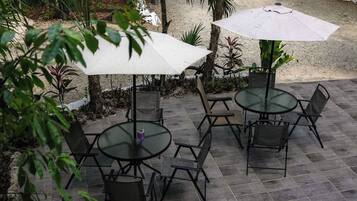 An outdoor patio with round tables and chairs, two umbrellas, and a gravel path.