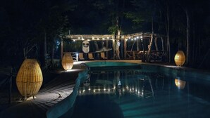 A nighttime pool area with a clear pool, string lights, and two large lantern-style lights. - Jolie Jungle Eco Hotel (Leona Vicario)