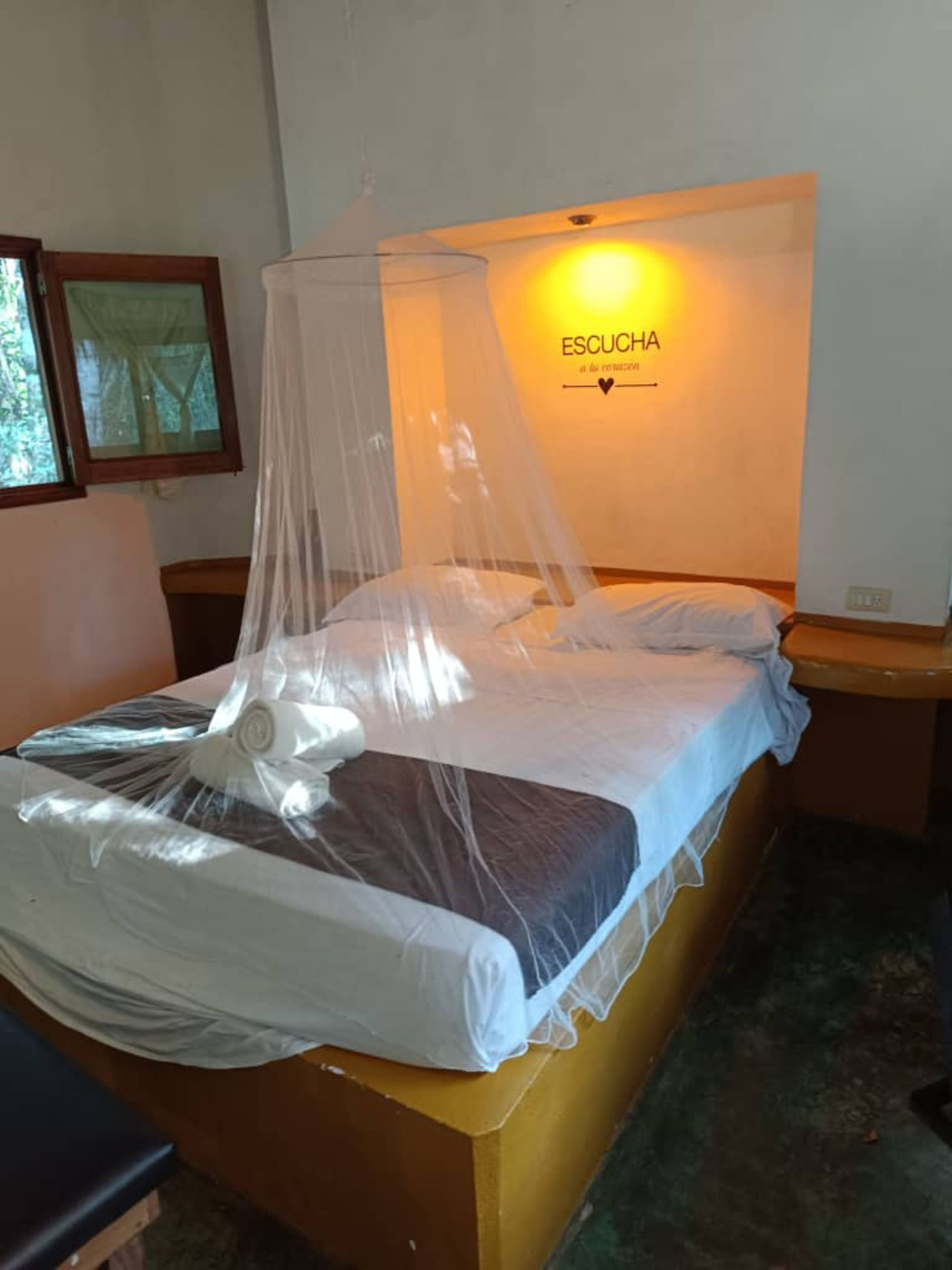 Una cama con mosquitero, una lámpara de pared y un cartel que dice 'ESCUCHA'.