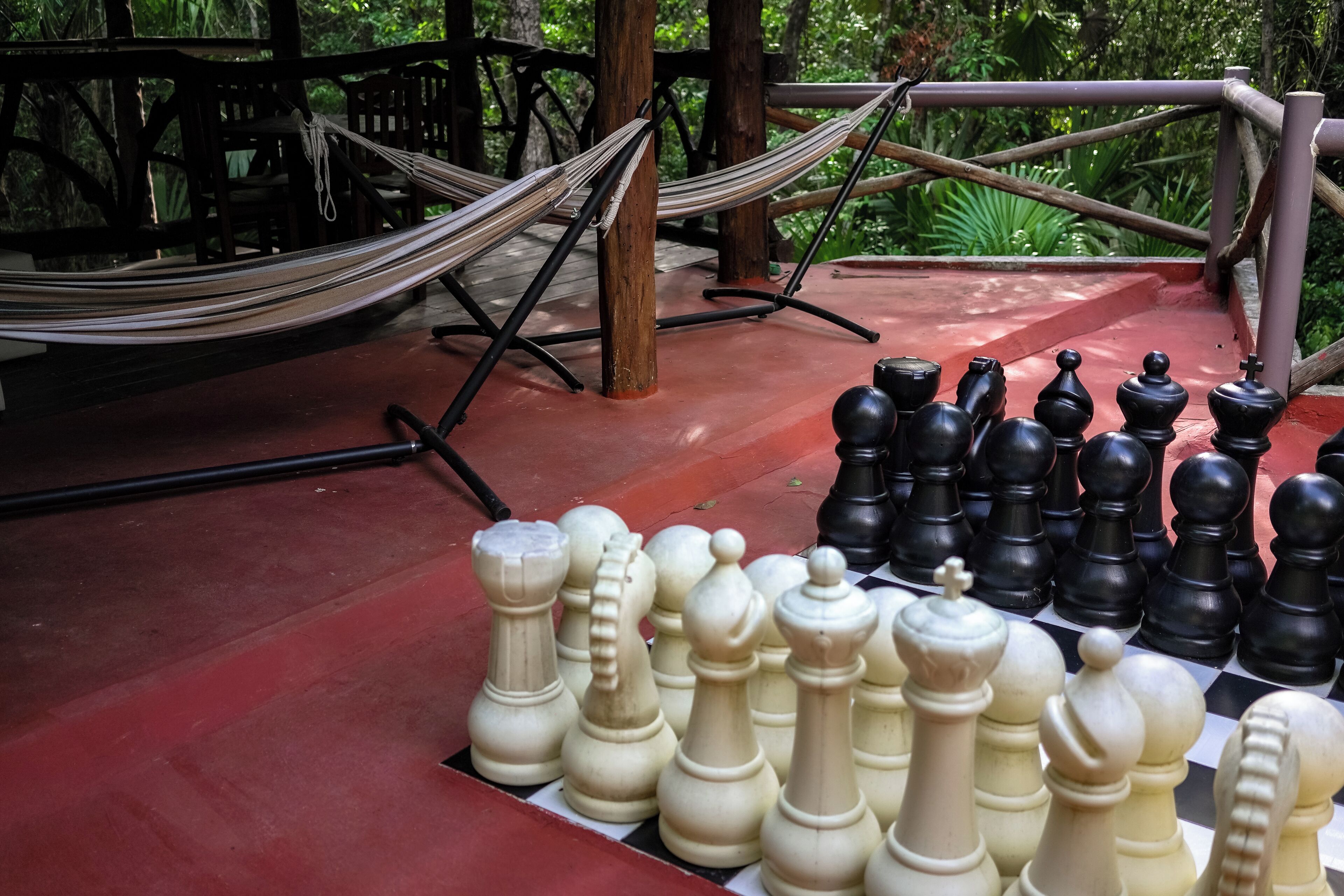 A chessboard set up on a red surface with a hammock and wooden furniture in the background.