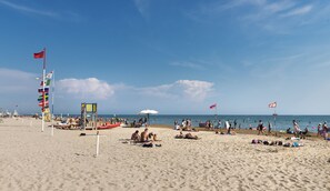A beach with flags, umbrellas, and people. - Princess Aparthotel (Bibione)
