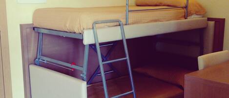 Una cama litera con escalera, un escritorio de madera y un tablón de anuncios en la pared.