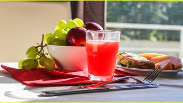 Une table avec un verre d’une boisson rouge, un saladier de fruits et des pâtisseries.