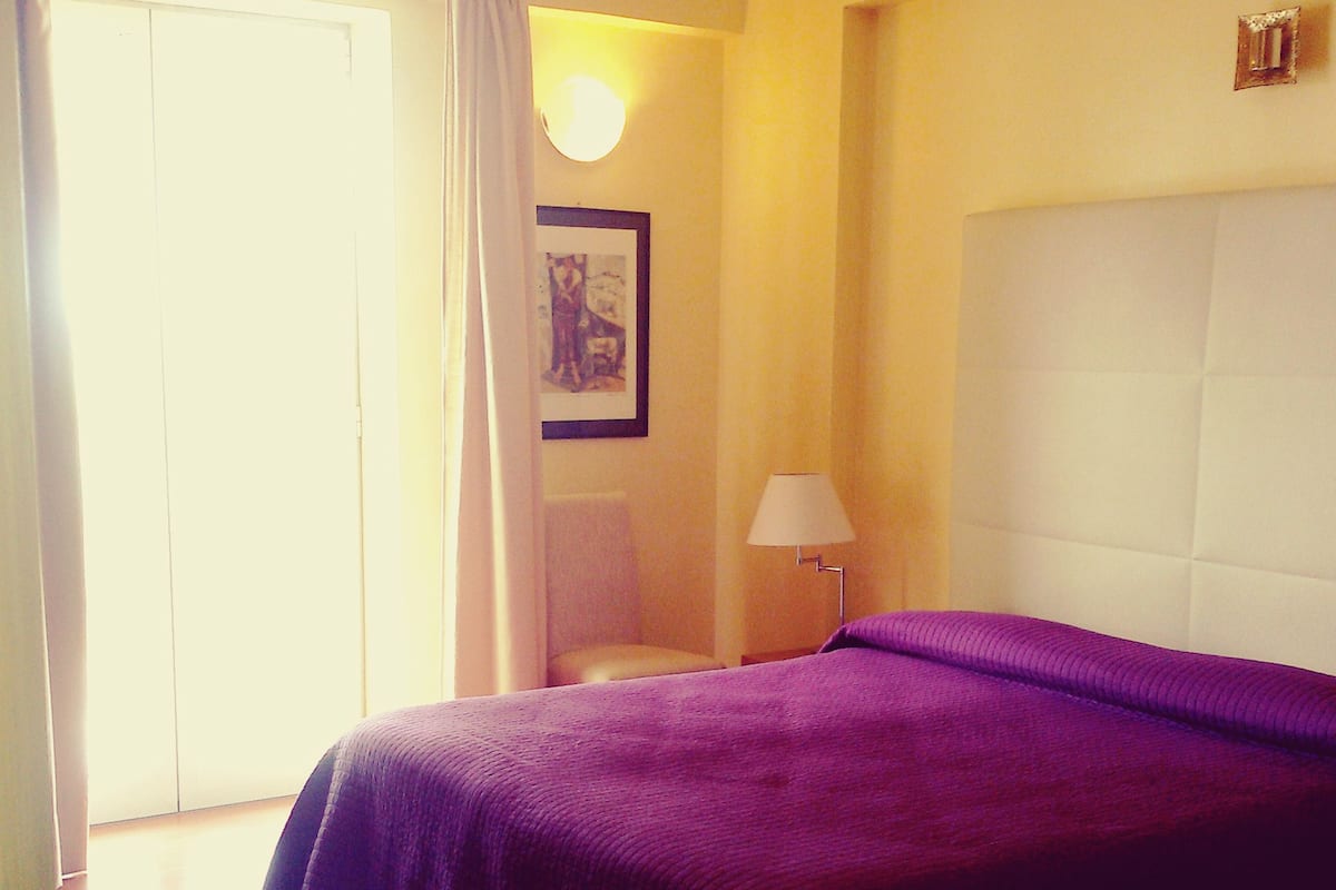 A hotel room with a bed, a chair, a lamp, and a framed picture on the wall.
