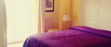 Een hotelkamer met een bed, een stoel, een lamp en een ingelijste foto aan de muur.