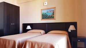 A hotel room with two beds, a dark wardrobe, a painting of a coastal scene, and a nightstand with a lamp. - Grand Hotel Paclà (Avola)