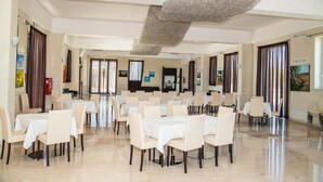 A spacious dining area with multiple tables and chairs, a high ceiling with a unique textured design, and artwork on the walls. - Grand Hotel Paclà (Avola)