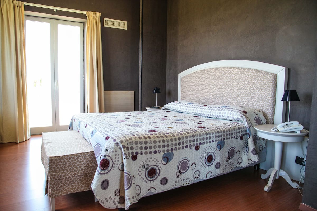 A bedroom with a large bed, bedside tables, a bench, and a view of the outdoors.