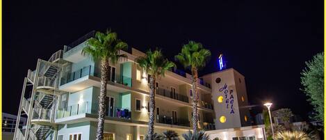 Un hotel de varios pisos con un diseño moderno, que cuenta con balcones, una escalera a la vista y una entrada bien iluminada.