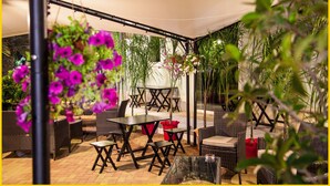 An outdoor patio area with wicker furniture, a table, and hanging plants. - Grand Hotel Paclà (Avola)