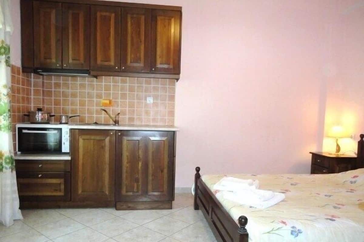 Un dormitorio compacto con cama, una kitchenette pequeña con microondas y una mesita de noche con lámpara.