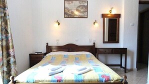 Un dormitorio con cama de madera, una mesita de noche, un escritorio, una silla, un espejo y un cuadro en la pared.