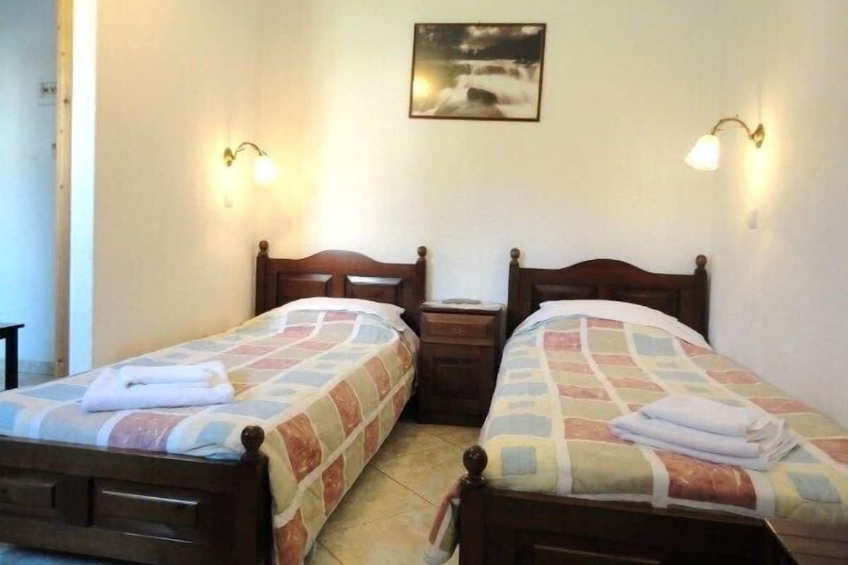 Una habitación con dos camas individuales, cada una con cabecero de madera y colcha acolchada. Hay mesitas de noche con lámparas y un cuadro enmarcado en la pared.