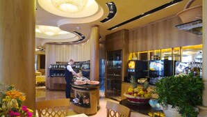A restaurant with a chef preparing food, a buffet counter with various dishes, and a fruit display. - Hotel Europa (San Michele al Tagliamento)