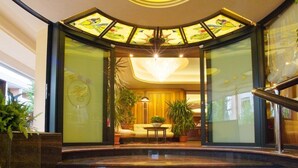 A hotel lobby with a curved glass entrance, a chandelier, and potted plants. - Hotel Europa (San Michele al Tagliamento)