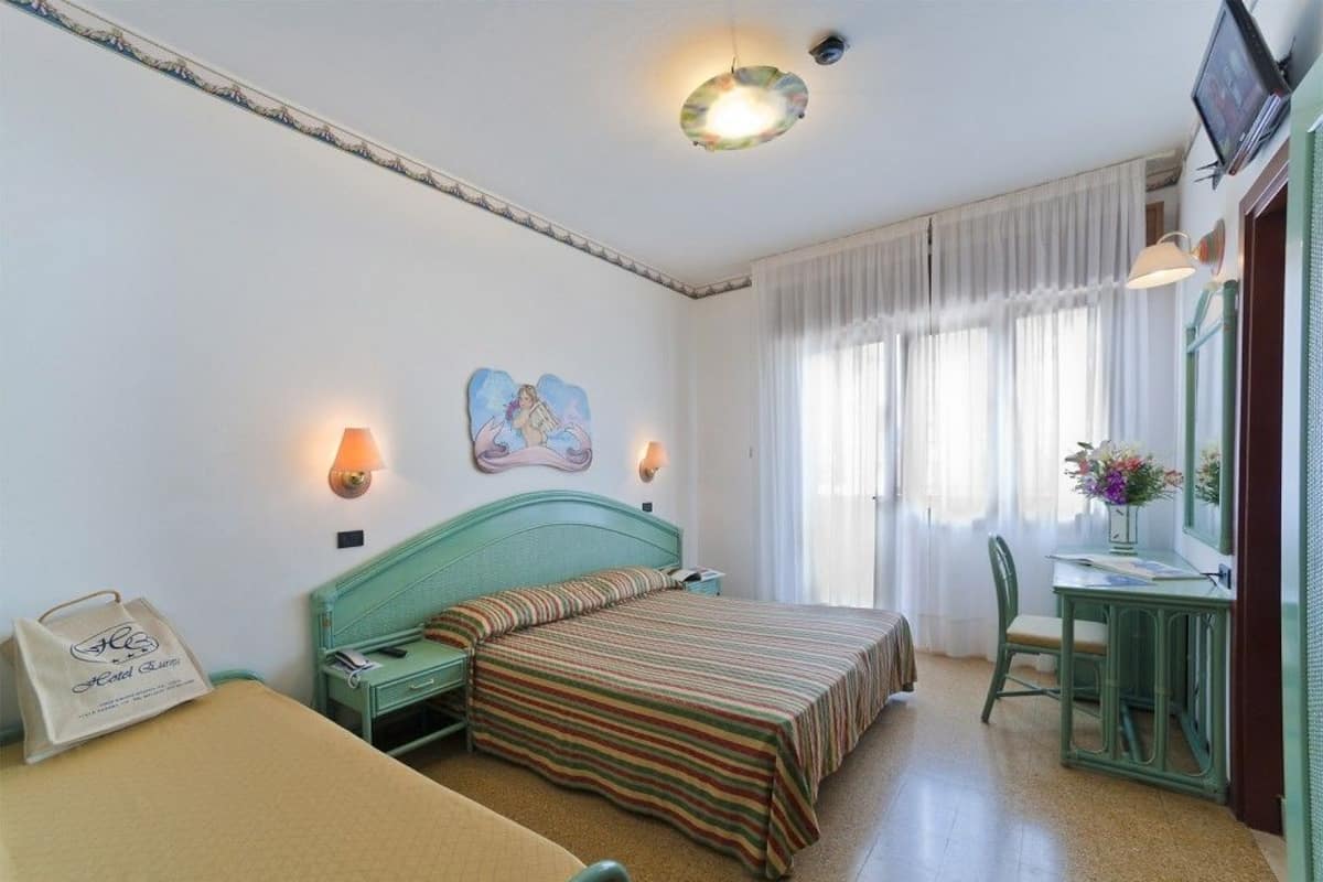 Une chambre d’hôtel avec un lit, un bureau et une chaise. Il y a un tableau accroché au mur et un sac posé sur le lit.