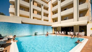 A swimming pool with lounge chairs and a building with multiple balconies in the background. - Hotel Europa (San Michele al Tagliamento)