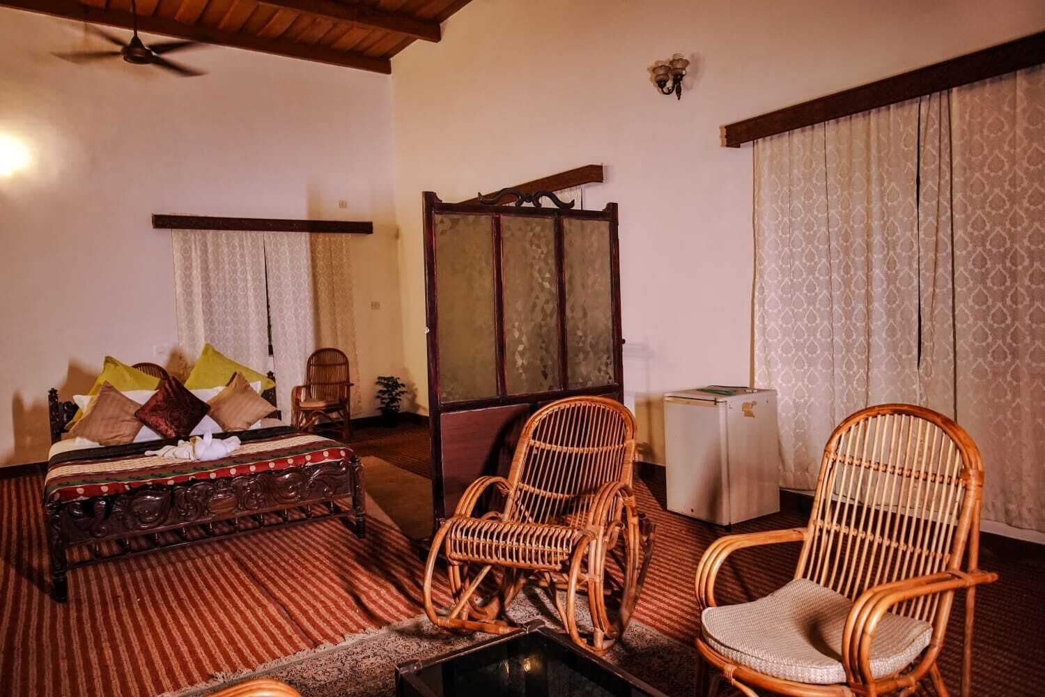 A room with a bed, two wicker chairs, a small table, and a cabinet.