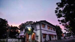 Un edificio de dos pisos con fachada blanca, entrada en arco y toldos rojos.