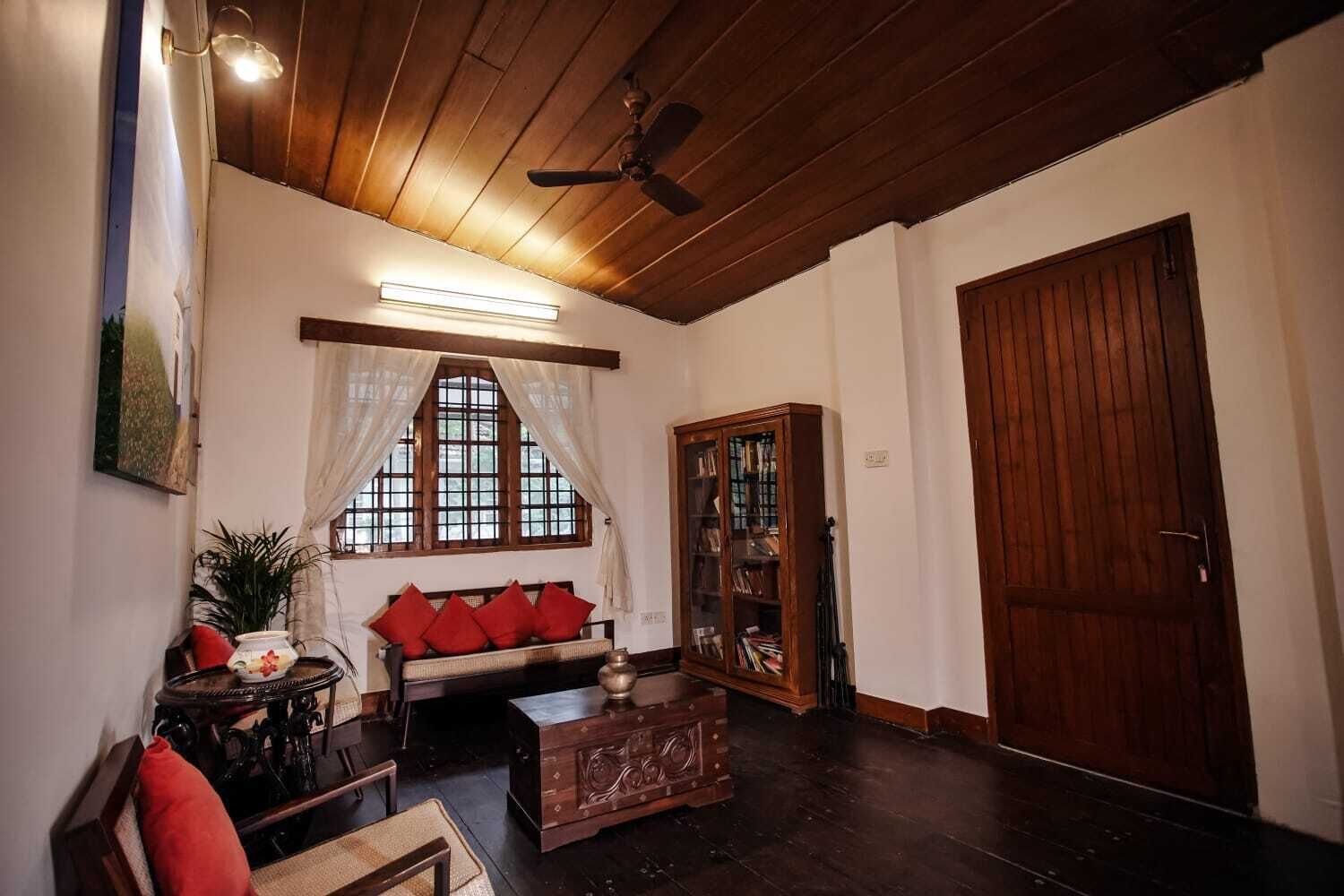 A room with a wooden ceiling, a ceiling fan, a large window with curtains, a wooden cabinet with glass doors, and a wooden door.