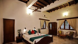 Un dormitorio con cama de madera, ventilador de techo, ventana con cortinas, armario de madera y una pequeña mesa con sillas.
