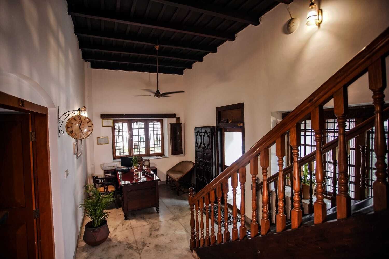 A spacious room with a wooden staircase, a ceiling fan, a desk with a chair, and a large window.
