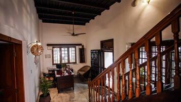 A spacious room with a wooden staircase, a ceiling fan, a desk with a chair, and a large window.