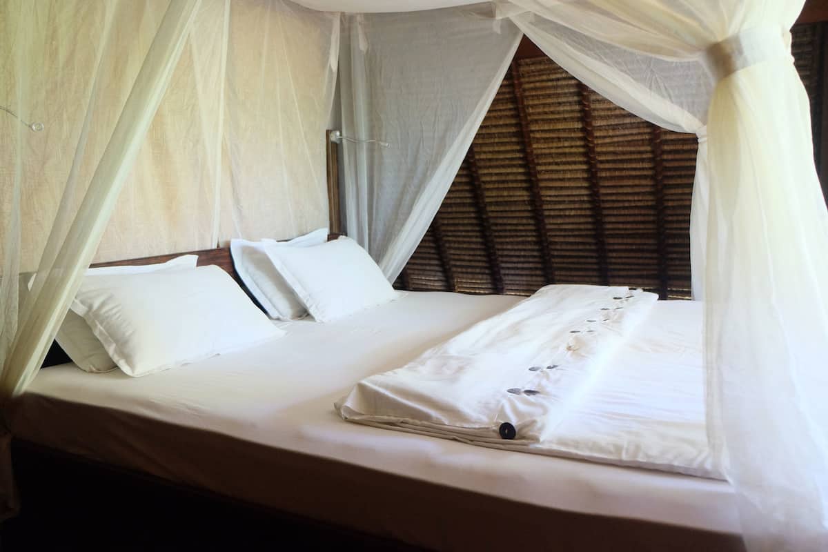A bed with a canopy, white bedding, and a wooden headboard.