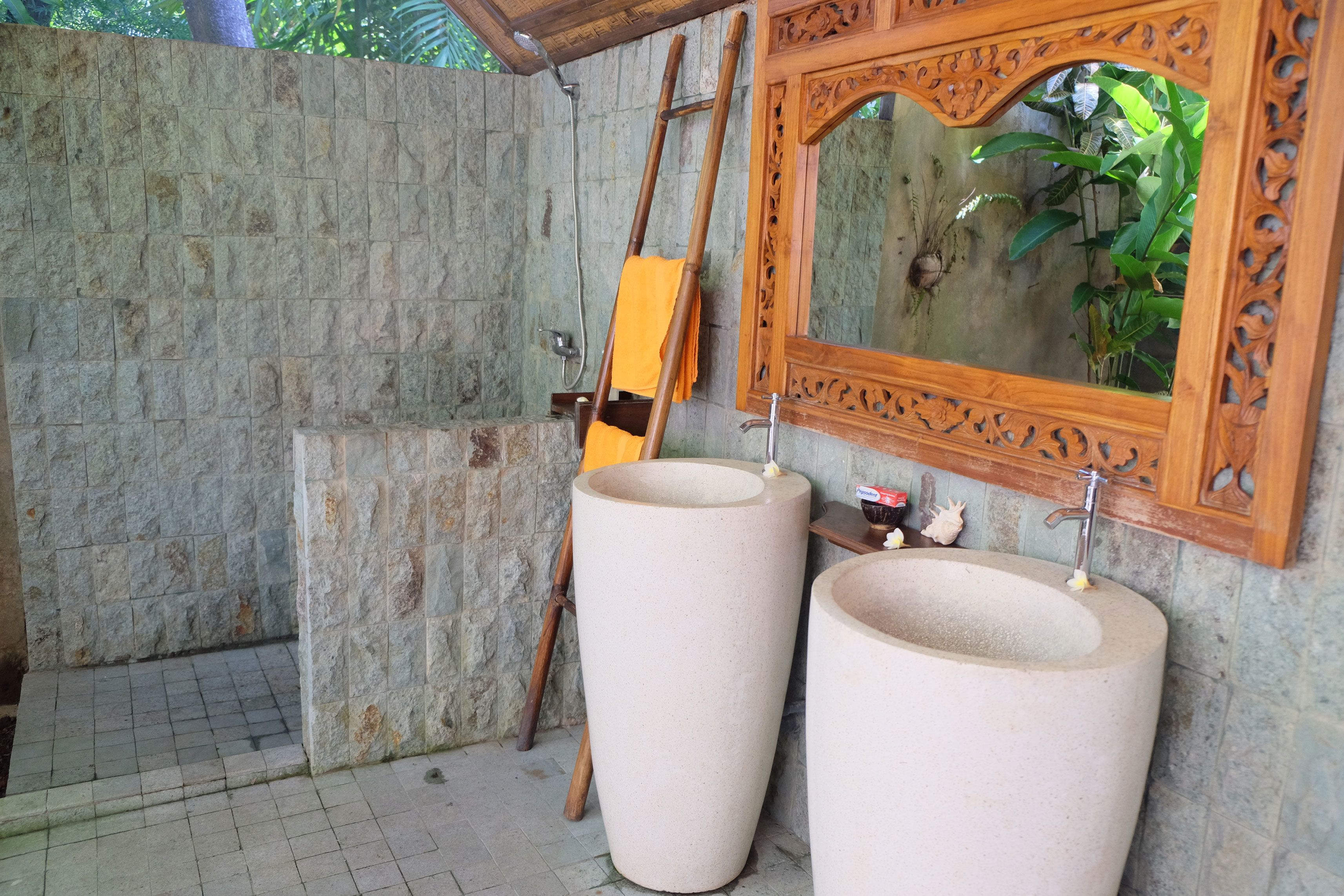 Een badkamer met twee grote stenen wasbakken, een houten ladder en een decoratieve spiegel.