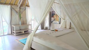 A bedroom with a canopy bed, wooden flooring, a small table, and a painting on the wall. - Villa Boreh Beach Resort and Spa (Tejakula)