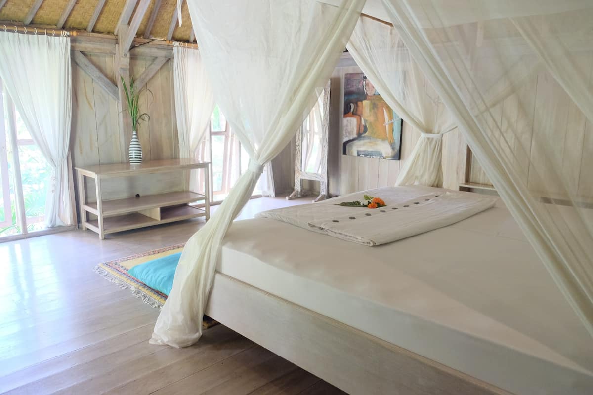 A bedroom with a canopy bed, wooden flooring, a small table, and a painting on the wall.