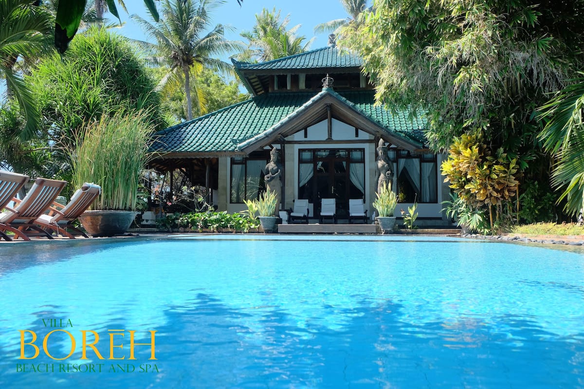 A poolside view of Villa Boreh with a traditional architectural style, a covered seating area, and lush tropical surroundings.