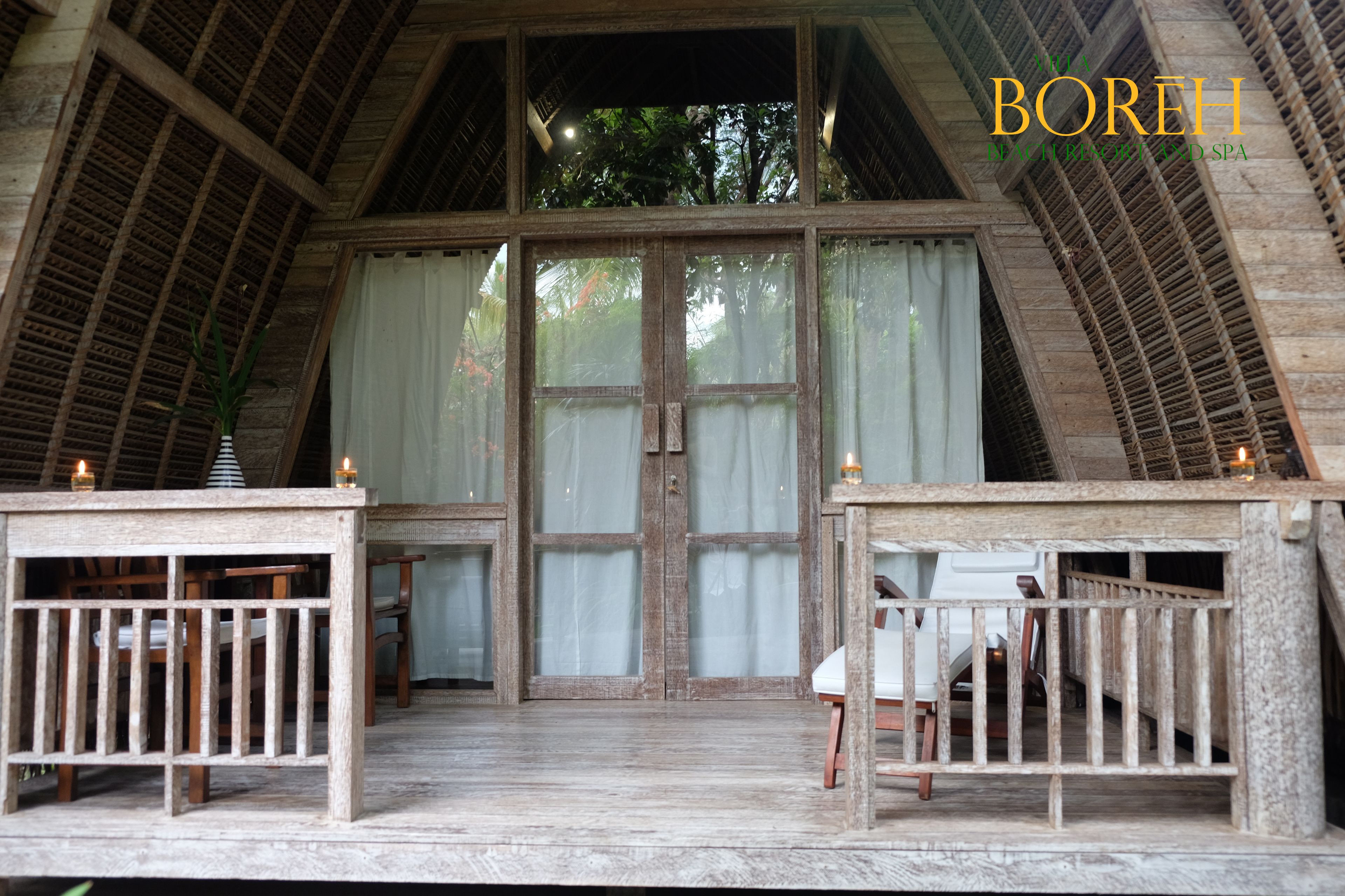 A rustic wooden room with a large wooden door, two small tables with candles, and a bench.