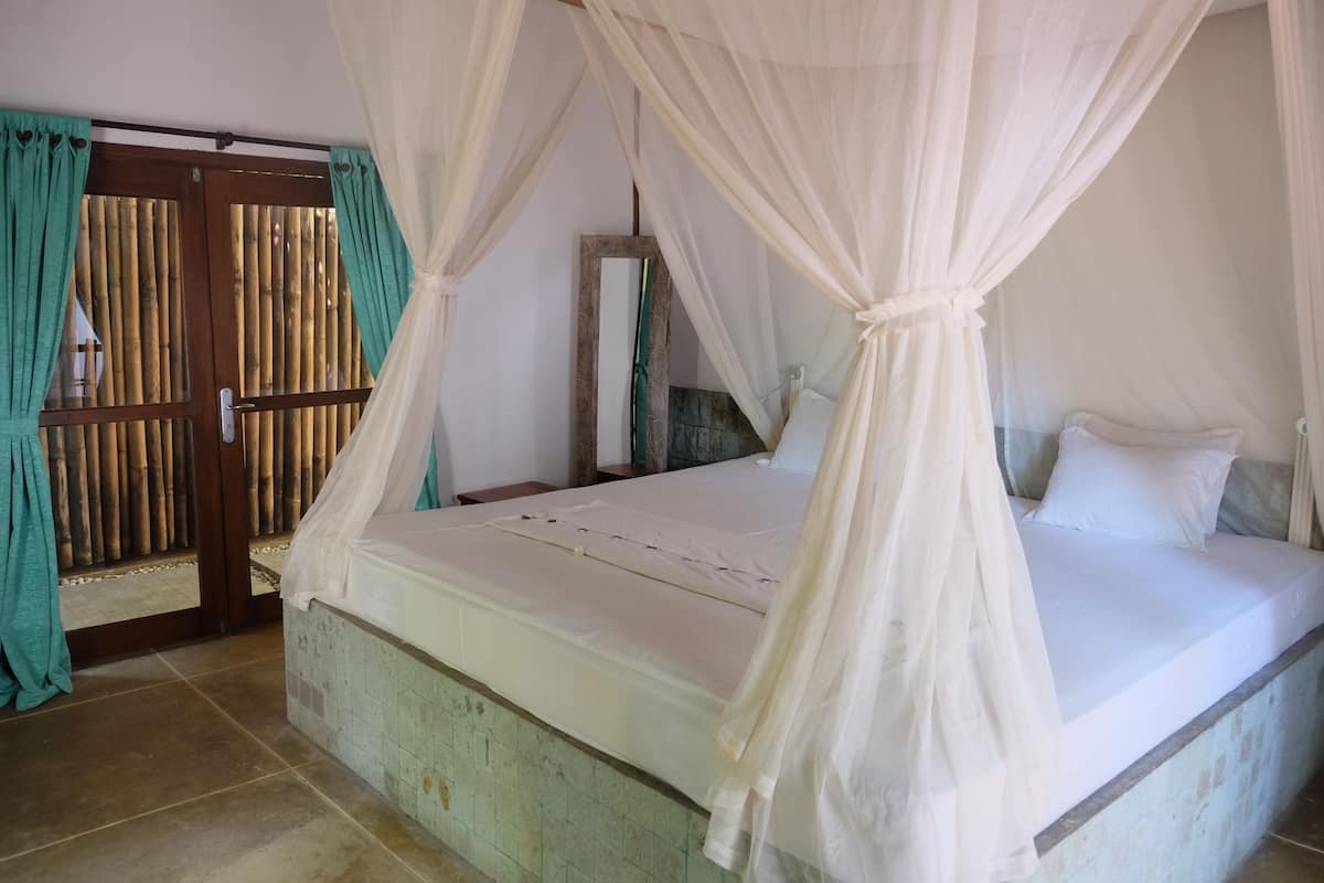A bed with a canopy, a wooden door with bamboo panels, and a tiled floor.