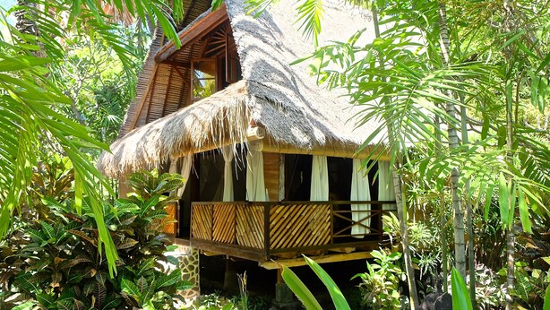 A thatched-roof bungalow surrounded by lush tropical foliage. - Villa Boreh Beach Resort and Spa (Tejakula)