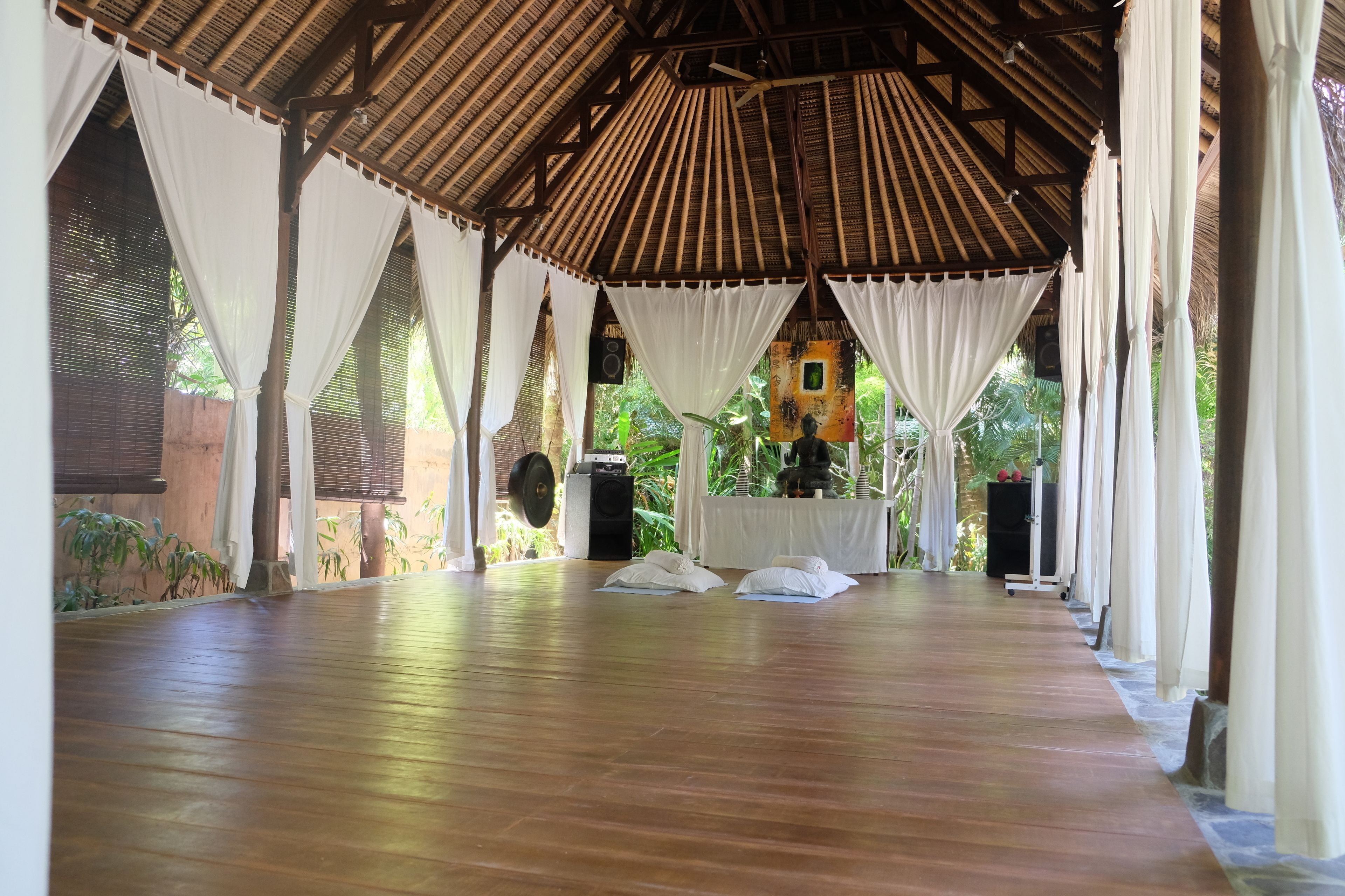 A covered outdoor area with a wooden floor, white curtains, and a speaker system.