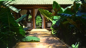 A wooden pathway leading to a traditional structure with a tiled roof, surrounded by lush tropical plants. - Villa Boreh Beach Resort and Spa (Tejakula)