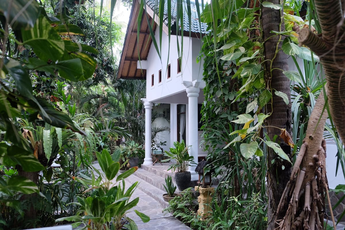 A white building with a tiled roof surrounded by lush greenery.