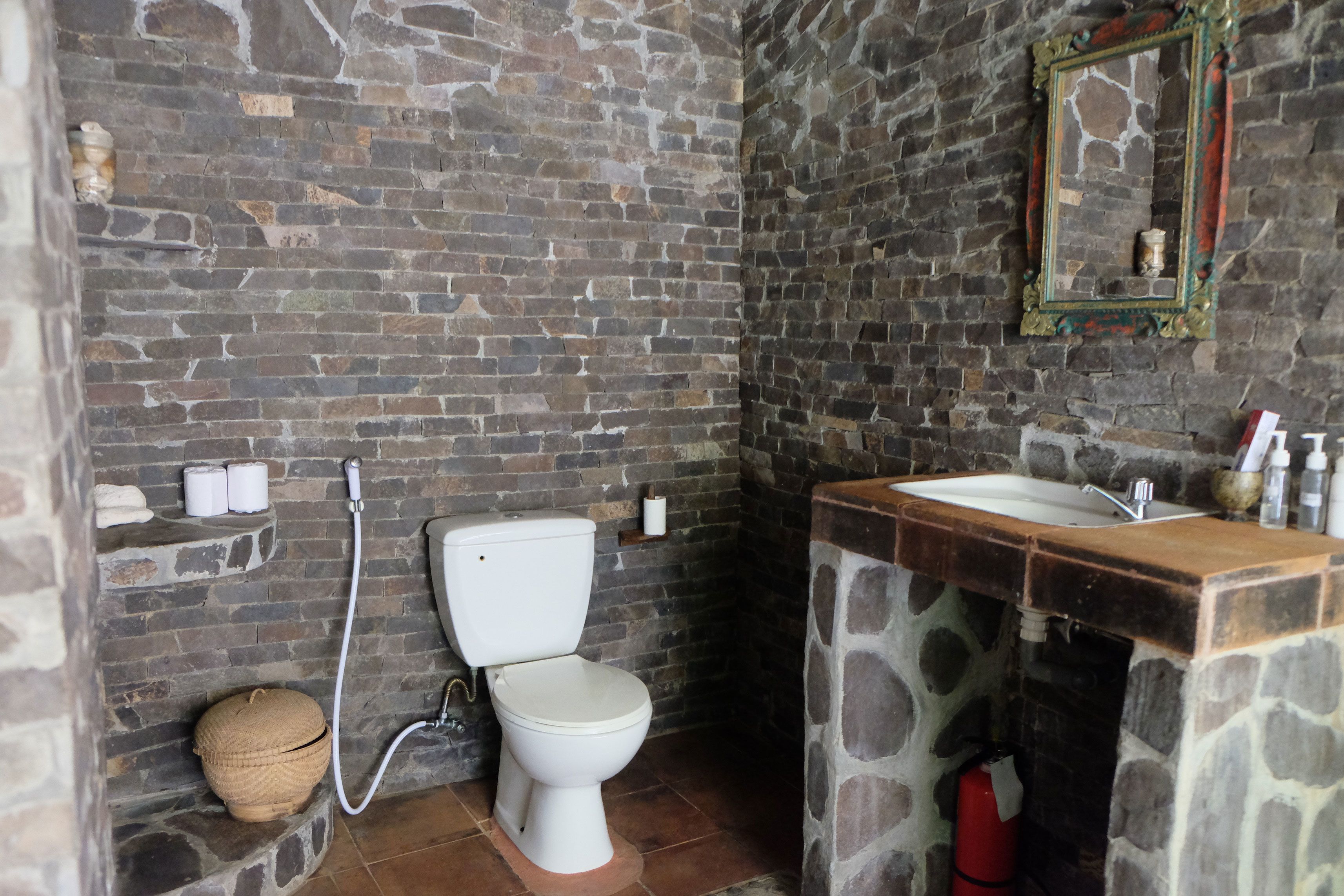 A bathroom with a stone sink, a toilet, and a mirror.