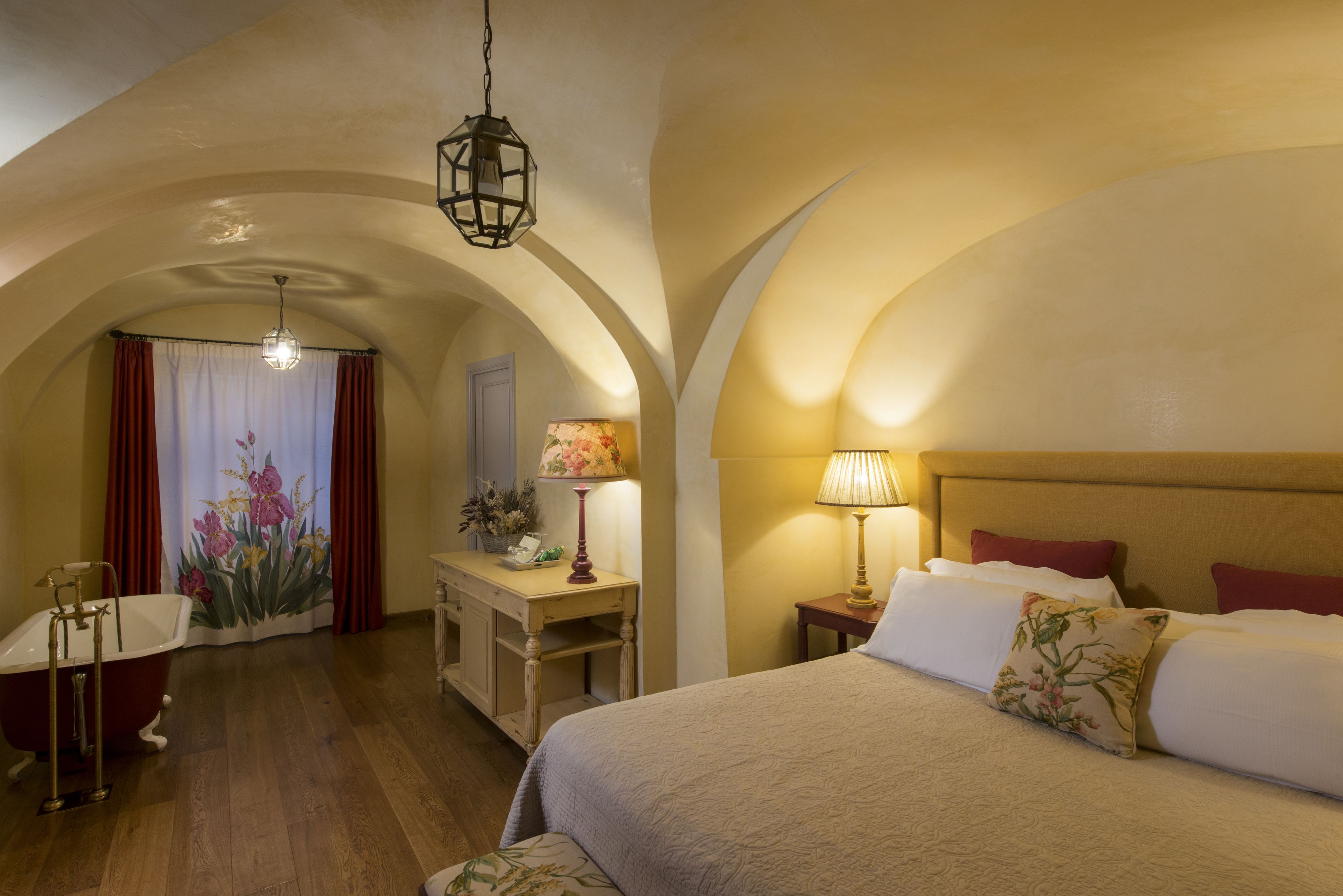 A hotel room with a large bed, a desk with a lamp, a vanity with a mirror, and a bathtub.