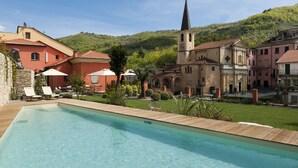 Una piscina con sillas de descanso, una iglesia y edificios con fachadas rojas y beige.