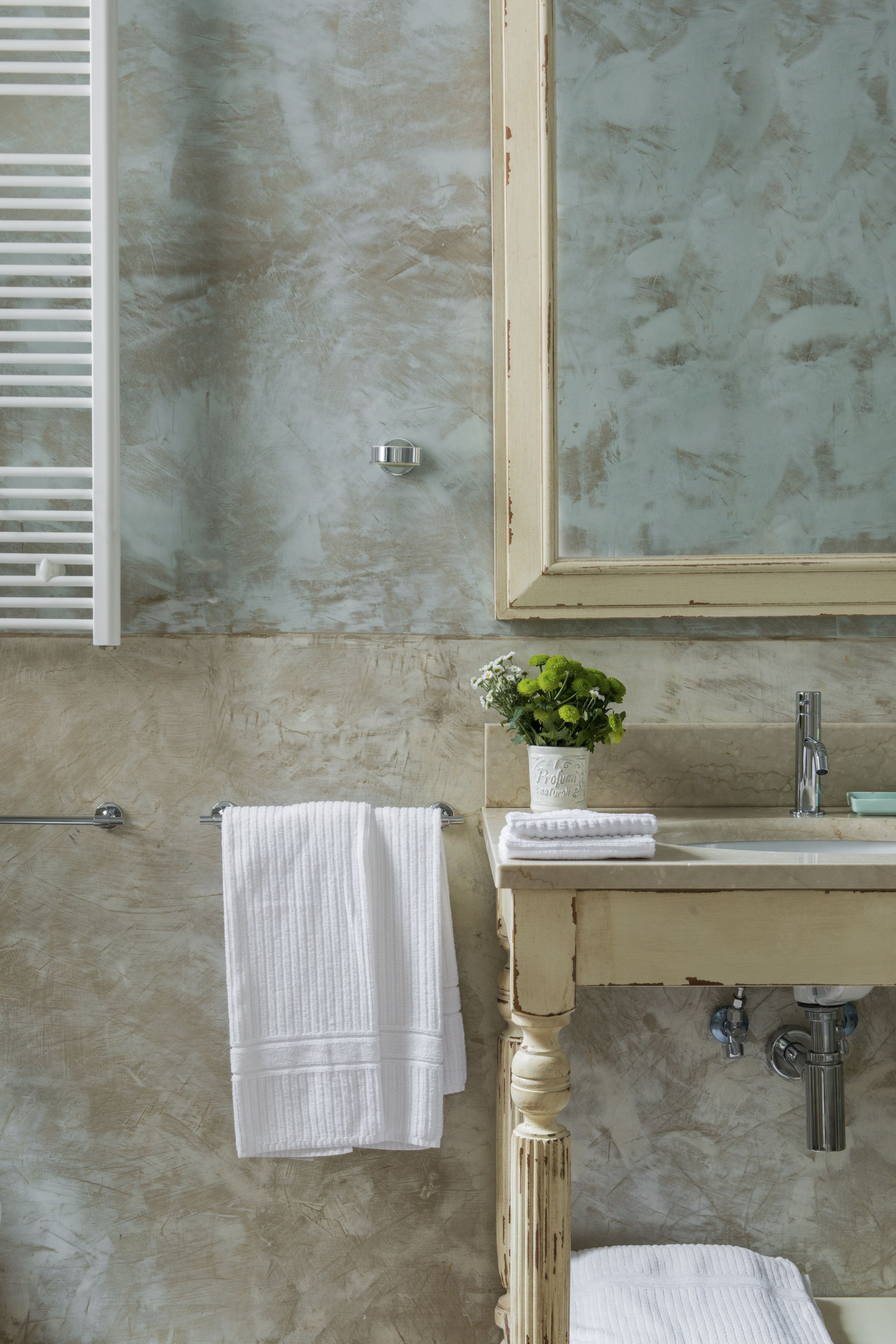 A bathroom with a marble wall, a wooden-framed mirror, a white sink, and a towel rack.