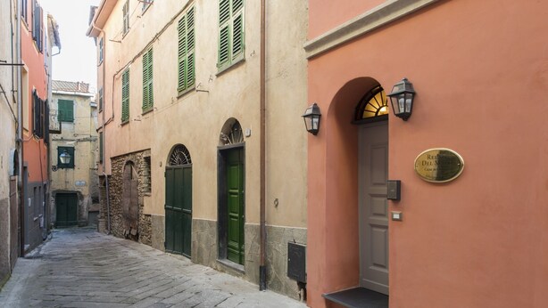 Una estrecha calle adoquinada flanqueada por edificios con contraventanas verdes y una puerta con un letrero que dice 